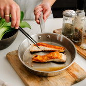 Zalm wordt gebakken in een roestvrijstalen koekenpan van 24 cm en omgedraaid met een keukenpincet