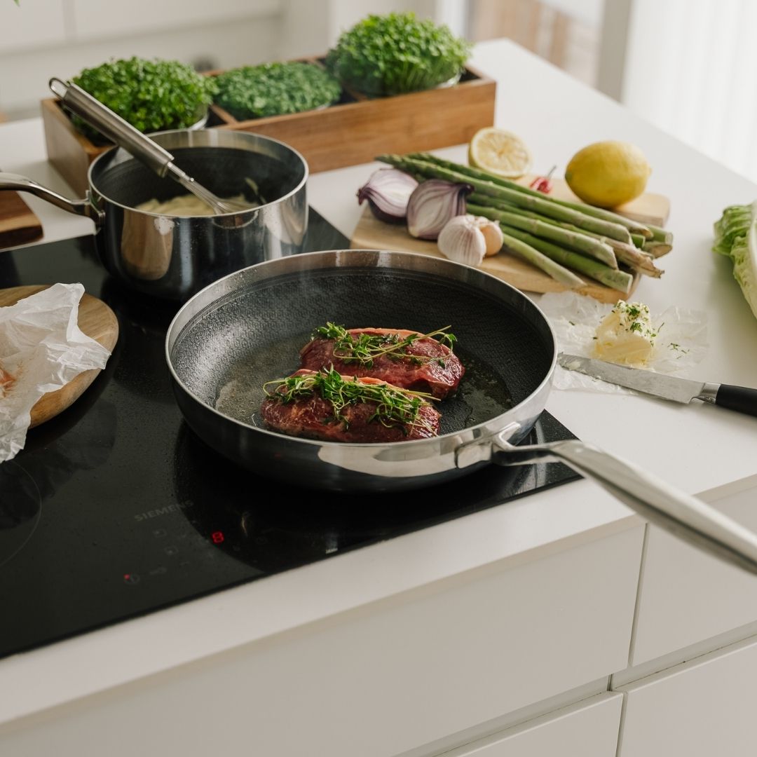 Koekenpan met steaks op een inductiekookplaat